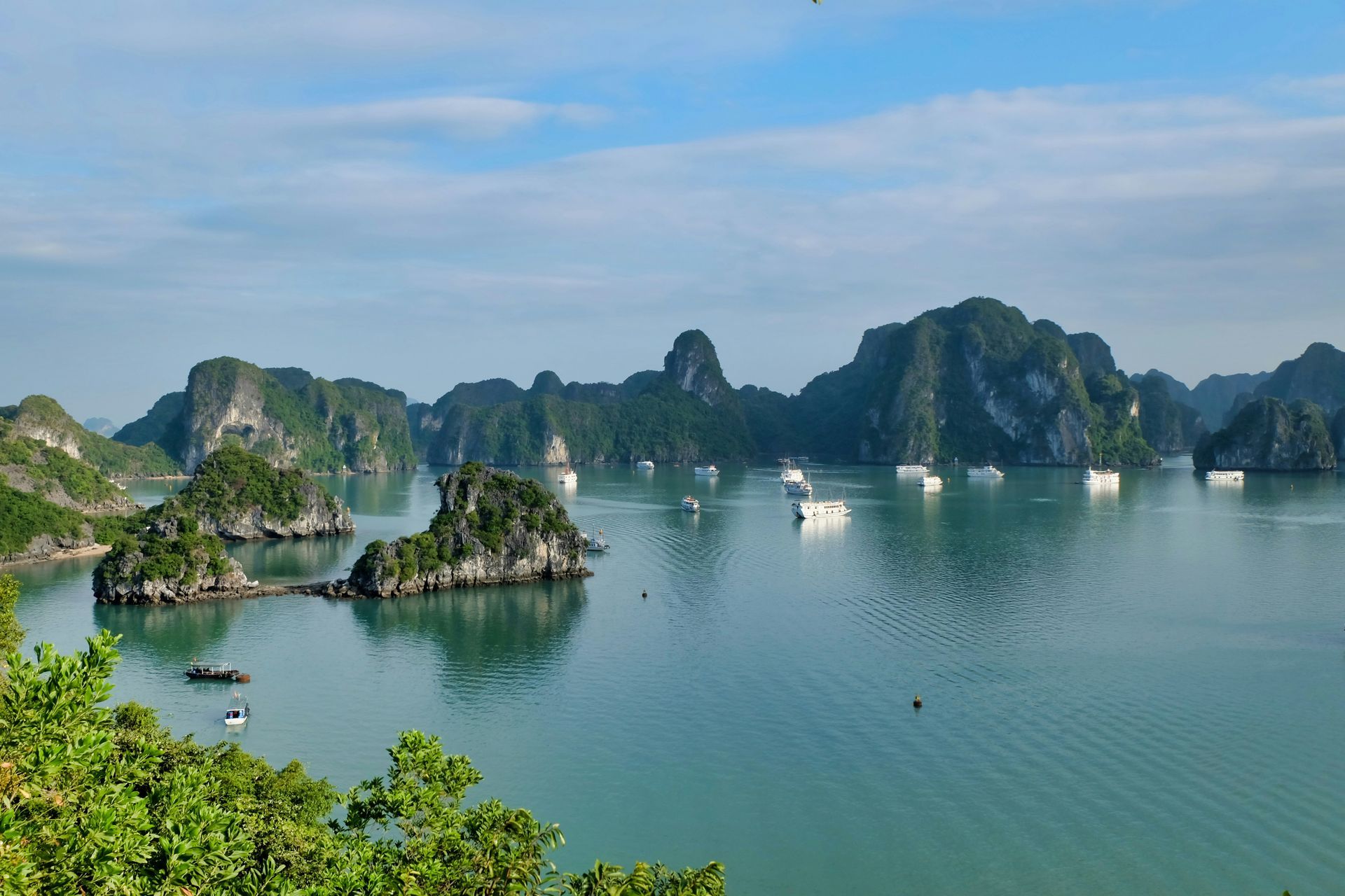 Ha Long Bay, Vietnam, featuring green, jagged limestone islands scattered across calm turquoise waters with several boats.