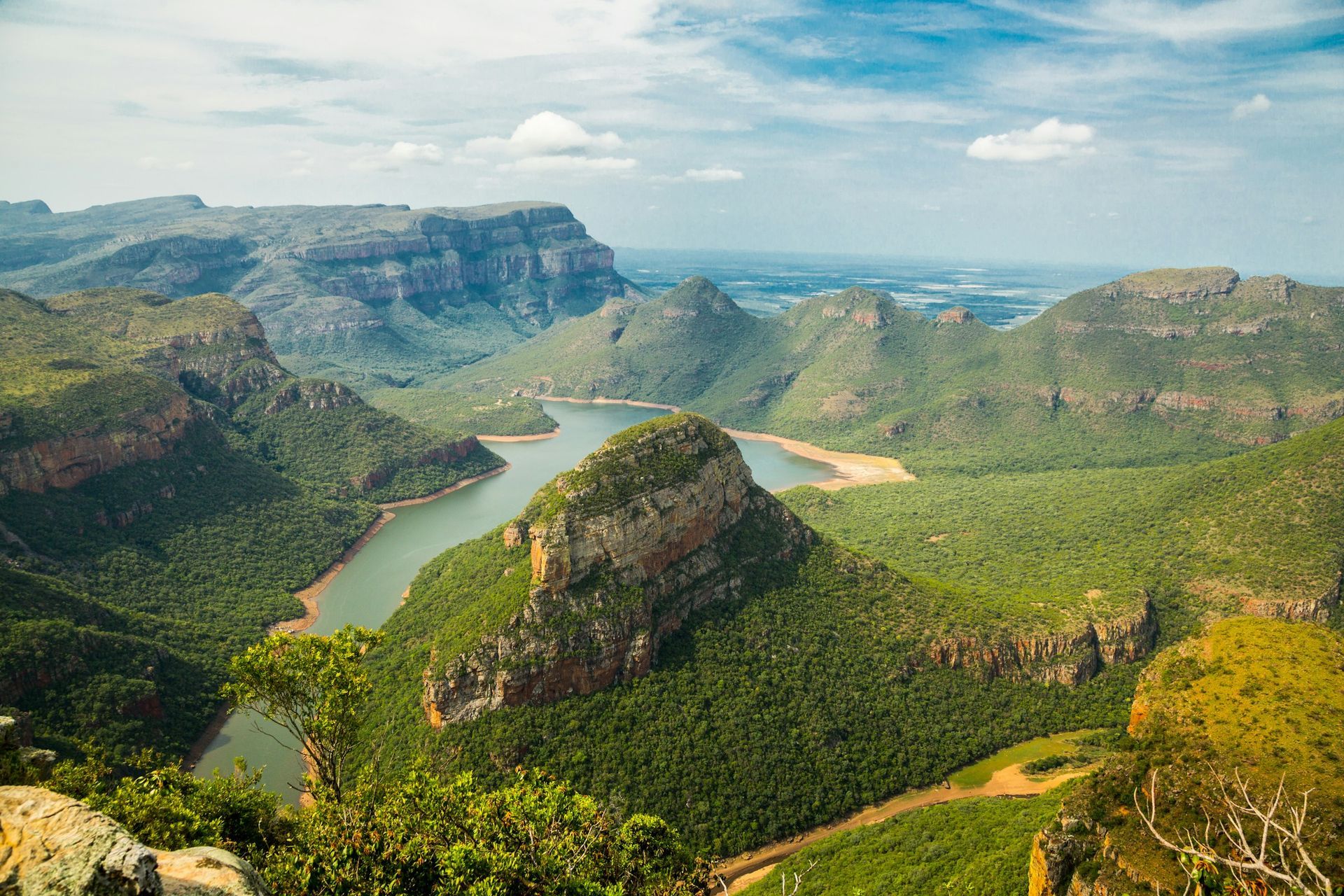 The Blyde River winds through the lush, mountainous landscape of the Blyde River Canyon in South Africa under a blue sky.