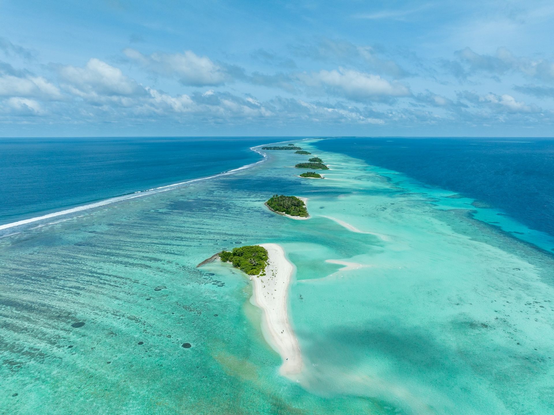 Aerial view of several small, lush green tropical islands surrounded by a vibrant turquoise reef in the middle of the ocean.