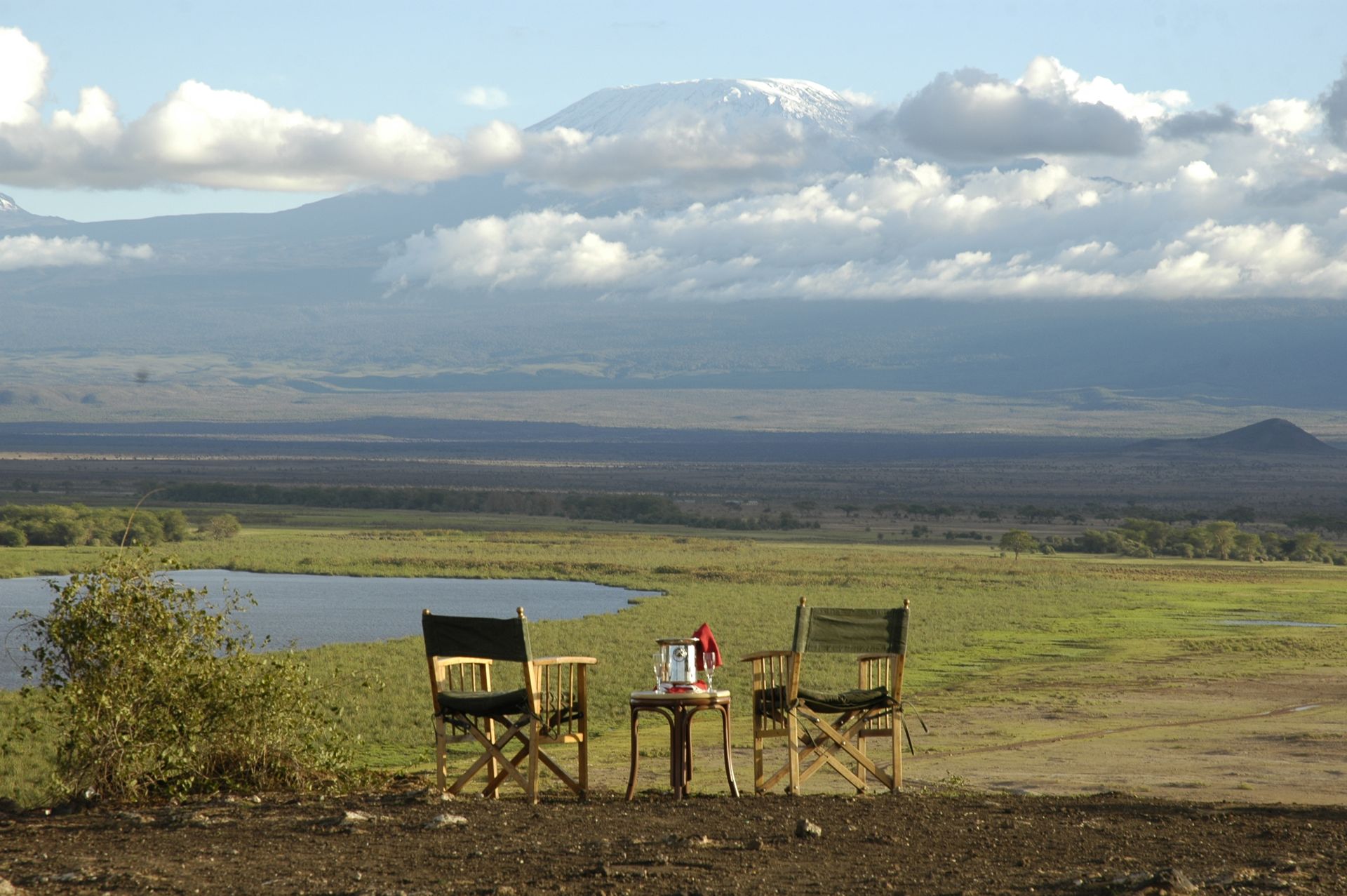 Two folding chairs and a small table overlooking a lush savanna landscape with a snow-capped mountain in the distance.