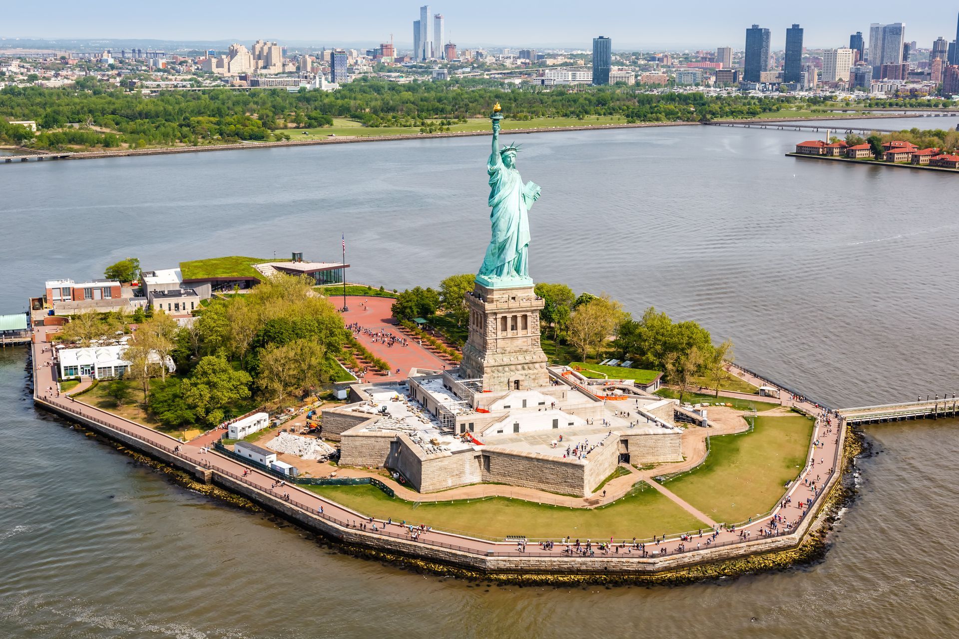 Aerial view of the Statue of Liberty on Liberty Island, surrounded by water with the New York City skyline in the distance.