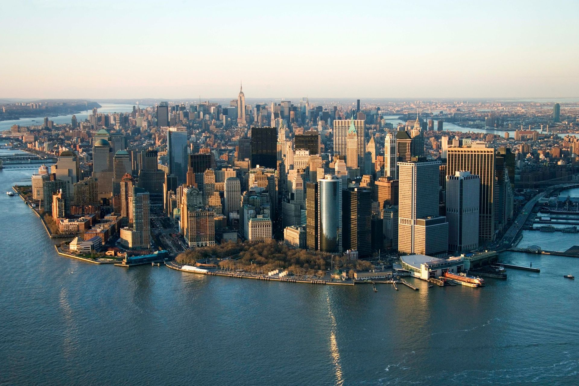 Aerial view of Manhattan’s skyline and the tip of Battery Park surrounded by water at sunset.