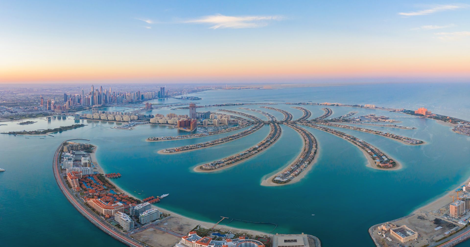 Aerial view of the man-made Palm Jumeirah archipelago in Dubai at sunset, surrounded by the blue waters of the Persian Gulf.