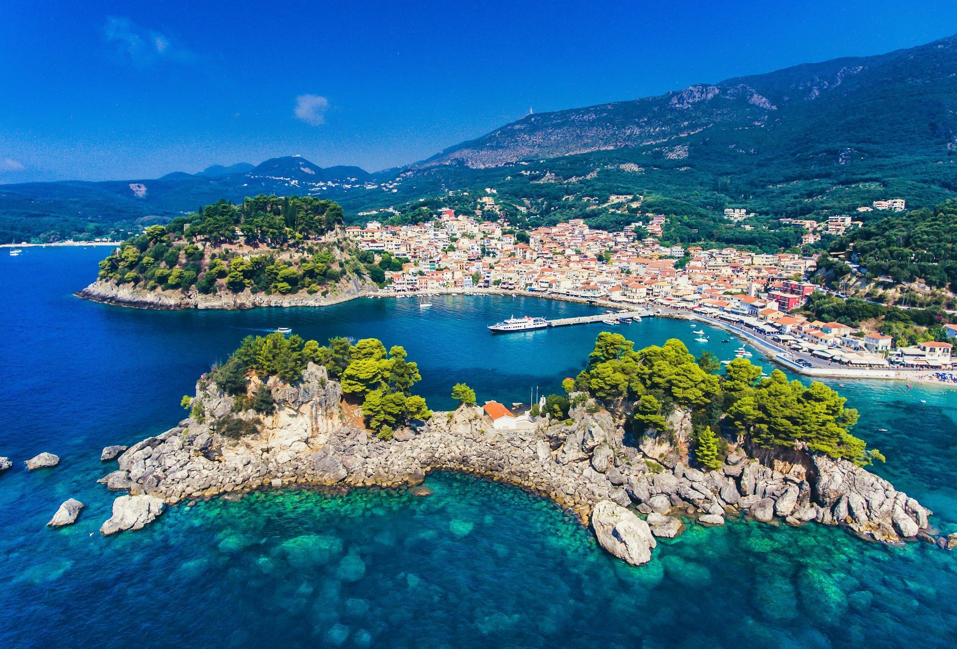 An aerial view of the rocky Panagia islet with a small white chapel, fronting the coastal town of Parga, Greece.