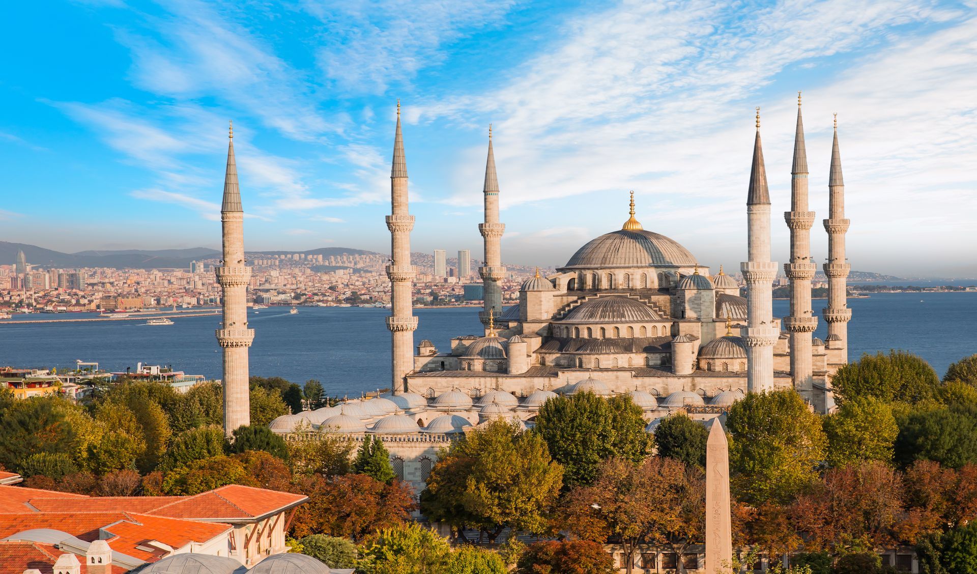 The Blue Mosque in Istanbul, with its six minarets and domed architecture, sits above trees by the Bosphorus strait.