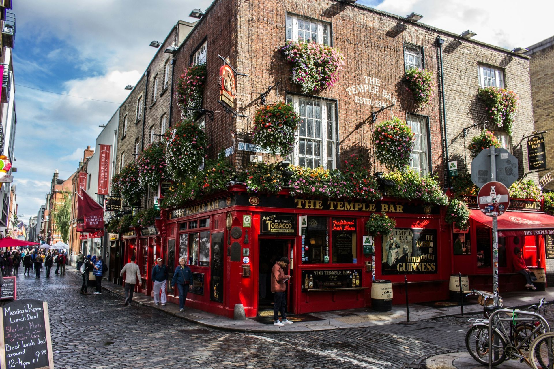 The iconic red exterior of The Temple Bar pub on a cobblestone street in Dublin, adorned with hanging flower baskets.