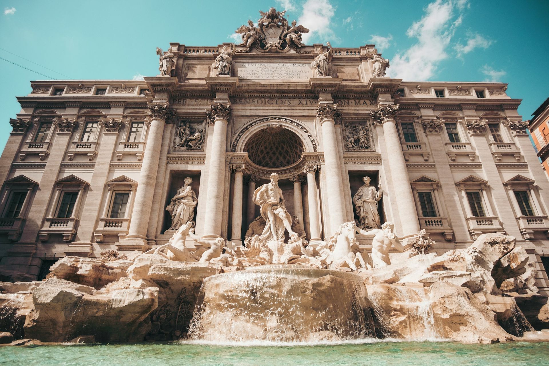 The Trevi Fountain in Rome, a grand baroque structure with ornate sculptures and water basins under a bright blue sky.