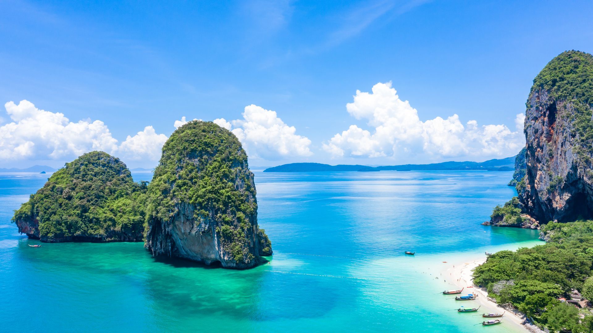 Aerial view of karst islands with lush green vegetation rising from vibrant turquoise water and a sandy beach.