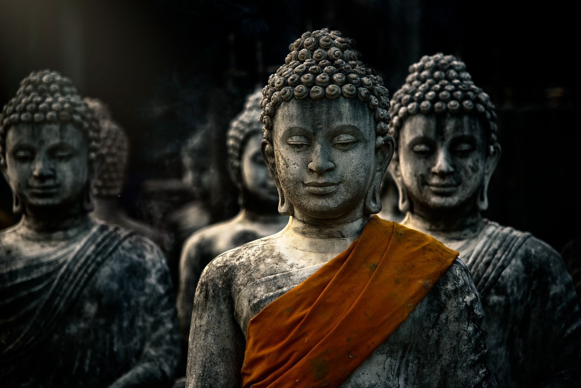 Several weathered stone Buddha statues with serene expressions, one wearing a bright orange sash.