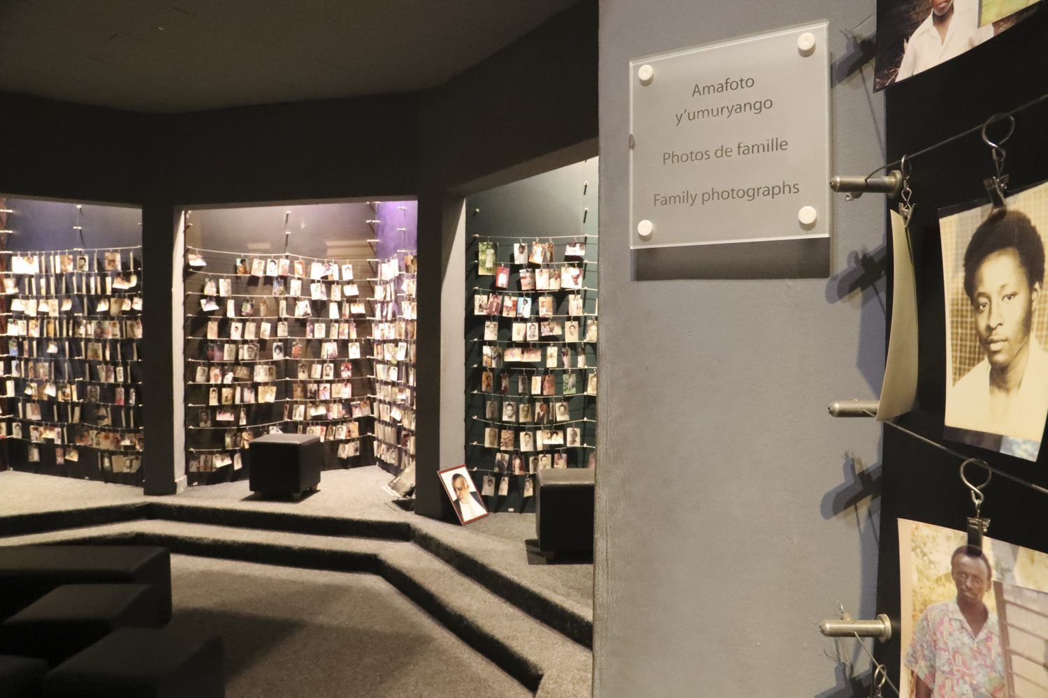 A library-style exhibit featuring rows of books on shelves, a sign on a gray pillar, and photos hanging on the right.