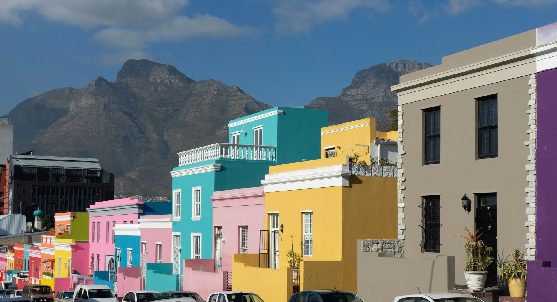 Brightly colored houses line a street in Cape Town's Bo-Kaap neighborhood, with Table Mountain rising in the background.