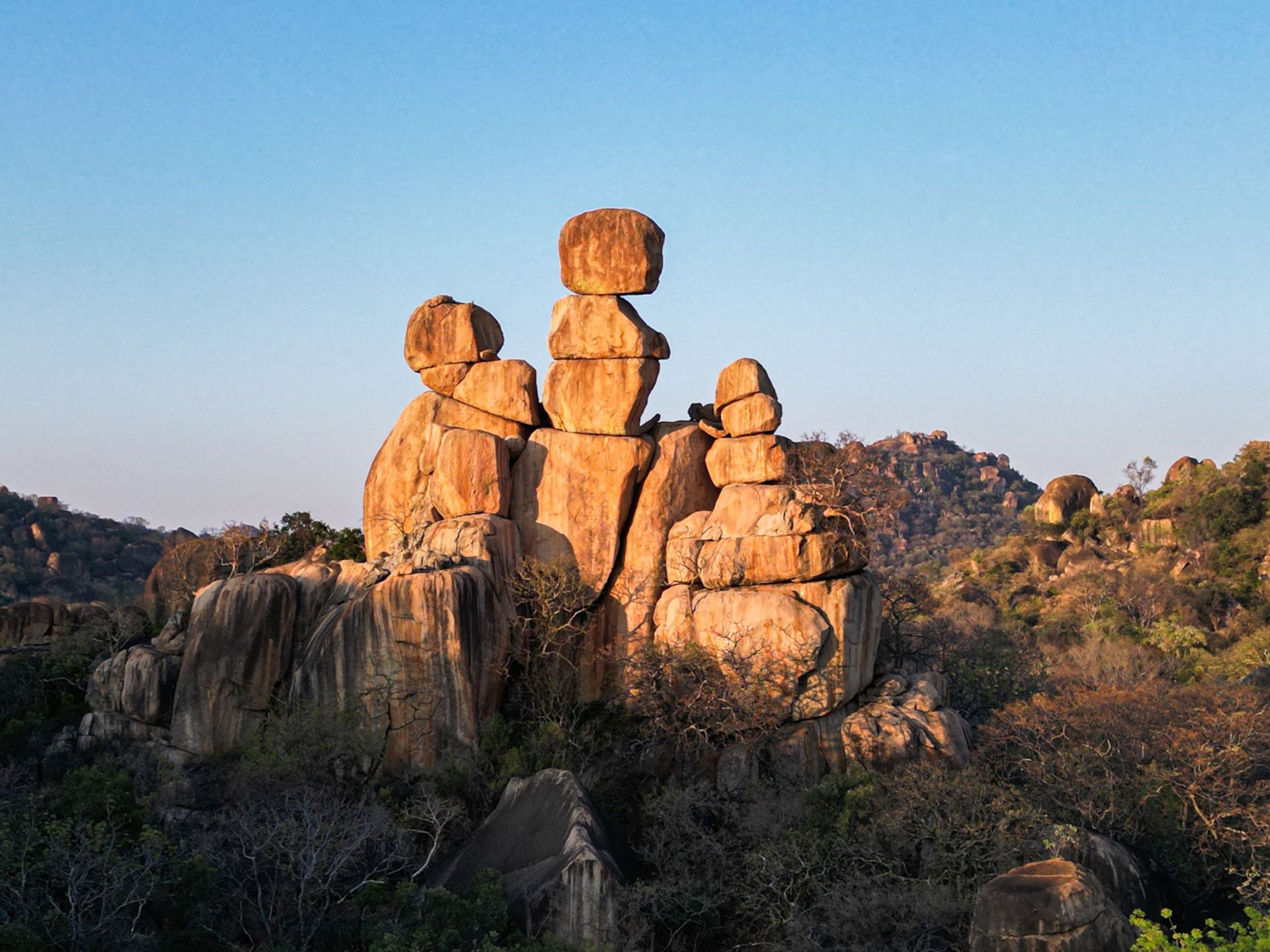 A cluster of balanced, golden-brown rock formations glowing in the light of the setting sun against a clear blue sky.