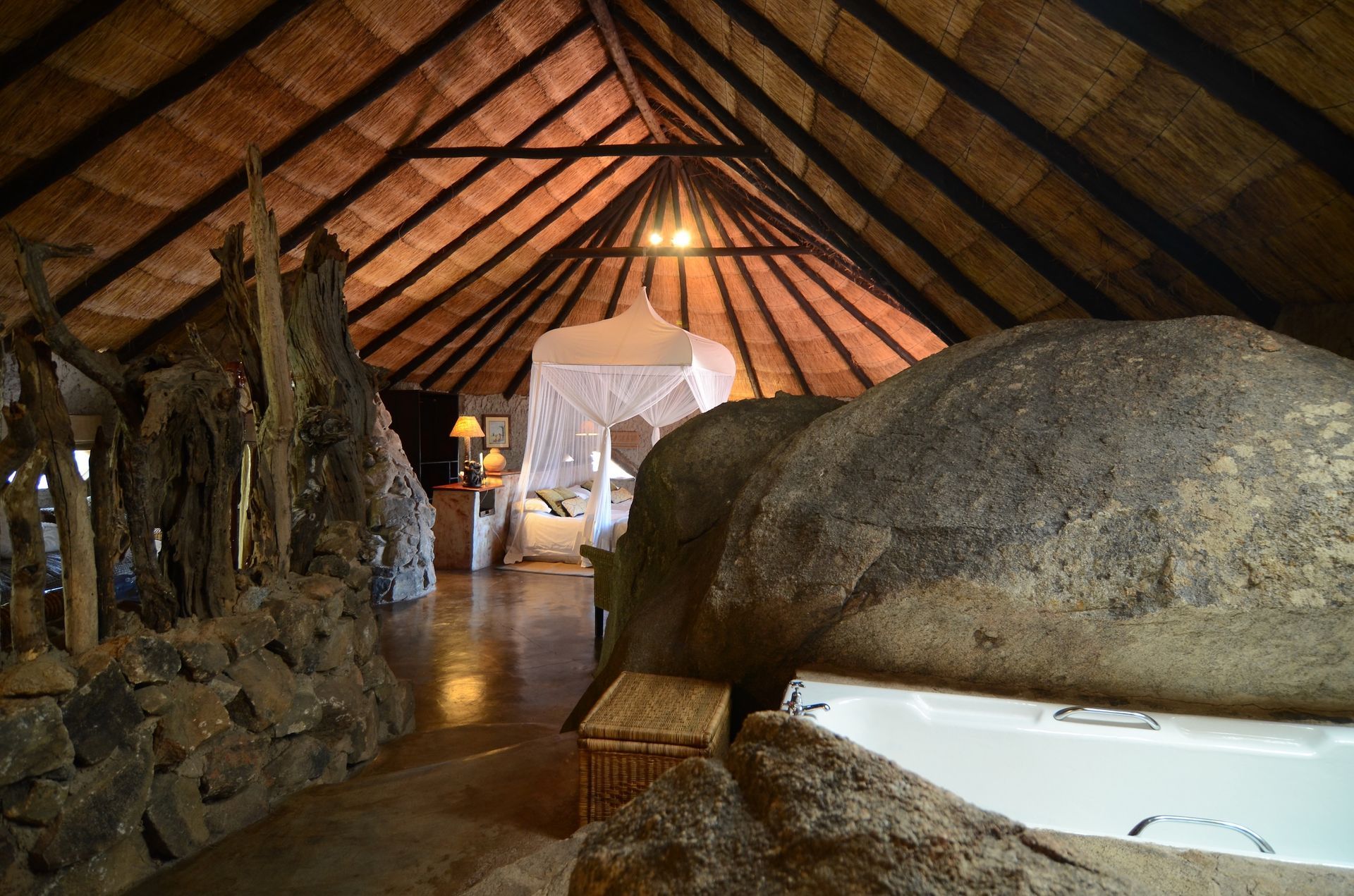 A unique luxury safari suite with a thatched roof, natural rock features, and a bed under a white mosquito net.