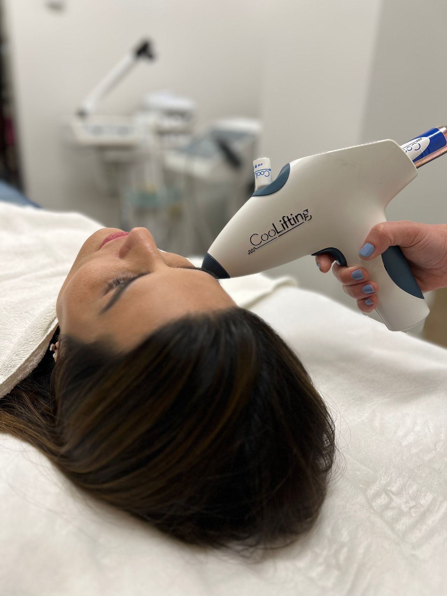 A woman is laying on a bed getting a laser treatment on her face.