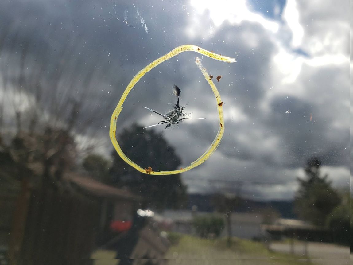 Broken window with a yellow-circled spiderweb crack against a cloudy outdoor scene