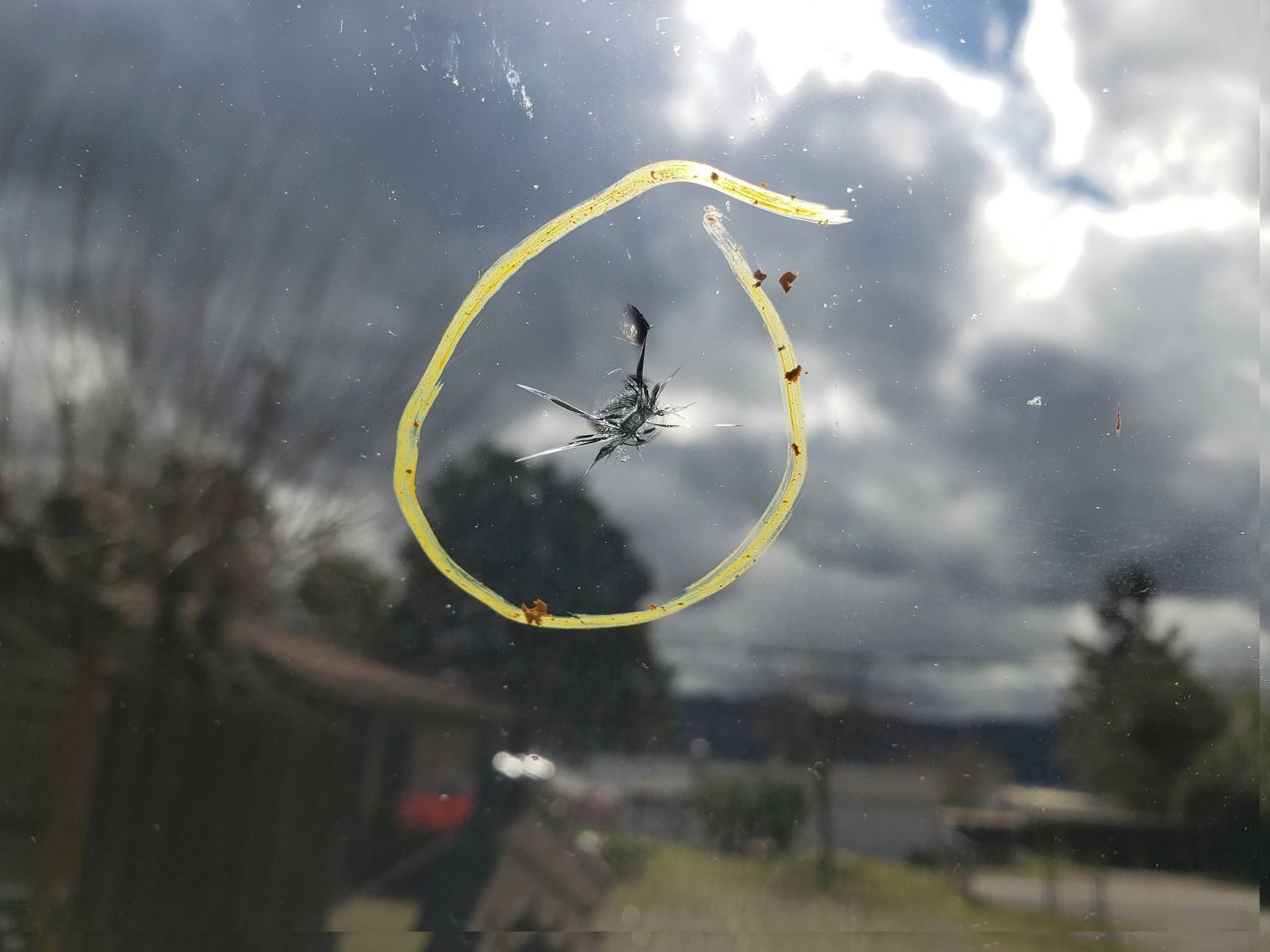 Broken window with a yellow-circled spider web crack against a cloudy outdoor background
