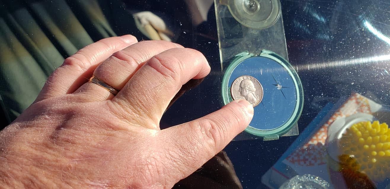 Hand holding a blue-taped compact disc on a reflective surface, with a small object centered on it.
