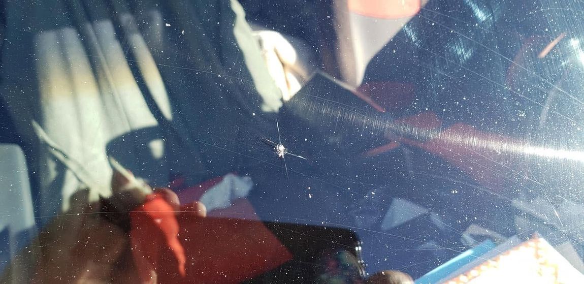 Close-up of a car interior with a sunlit windshield and seatbelt visible, partially obscured by reflections