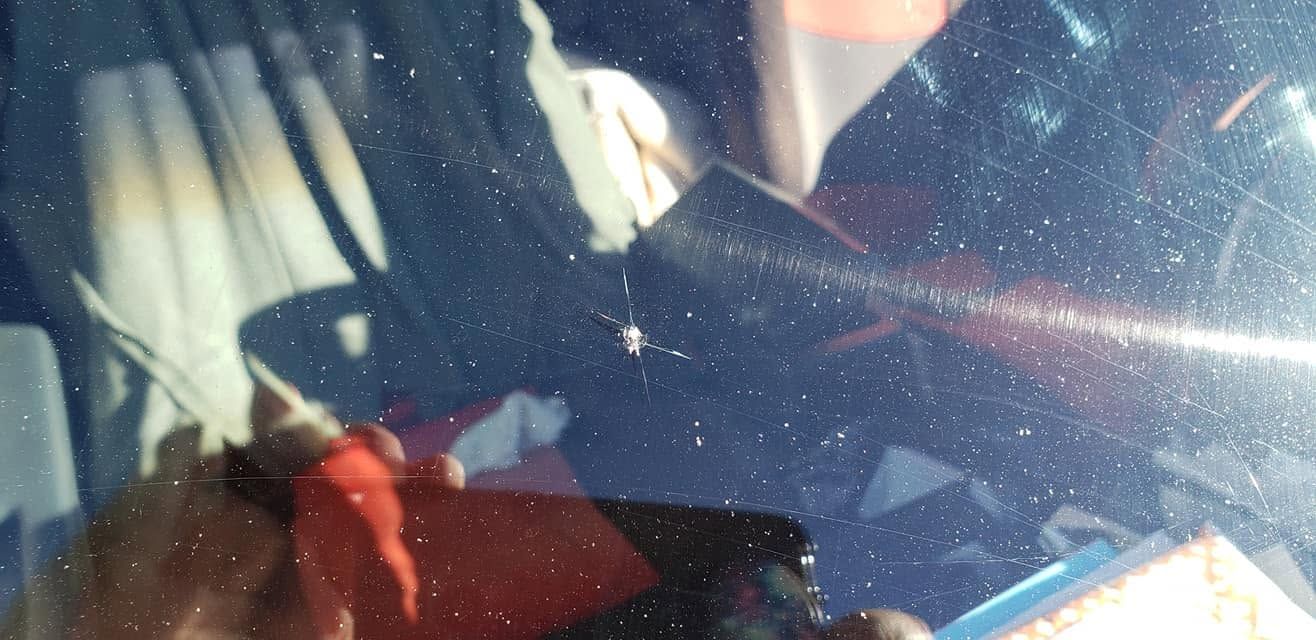 Close-up of a car interior with a sunlit windshield and seatbelt visible, partially obscured by reflections