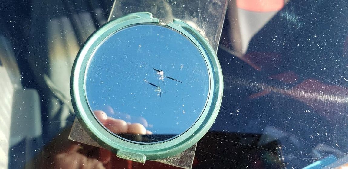 Close-up of a blue circular lens or mirror with small cracks, reflecting a hand and car interior