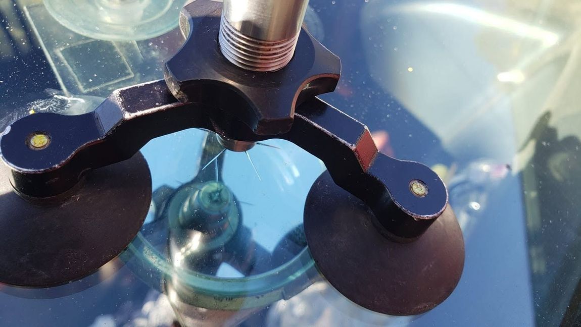 Close-up of a suction-cup windshield mount with a metal hinge on a glass surface