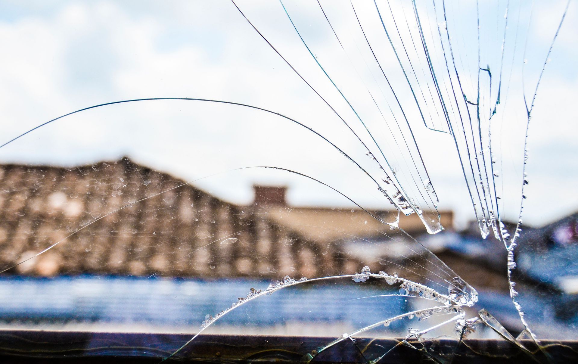 Cracked window with spiderweb fractures, blurred rooftop visible in the background