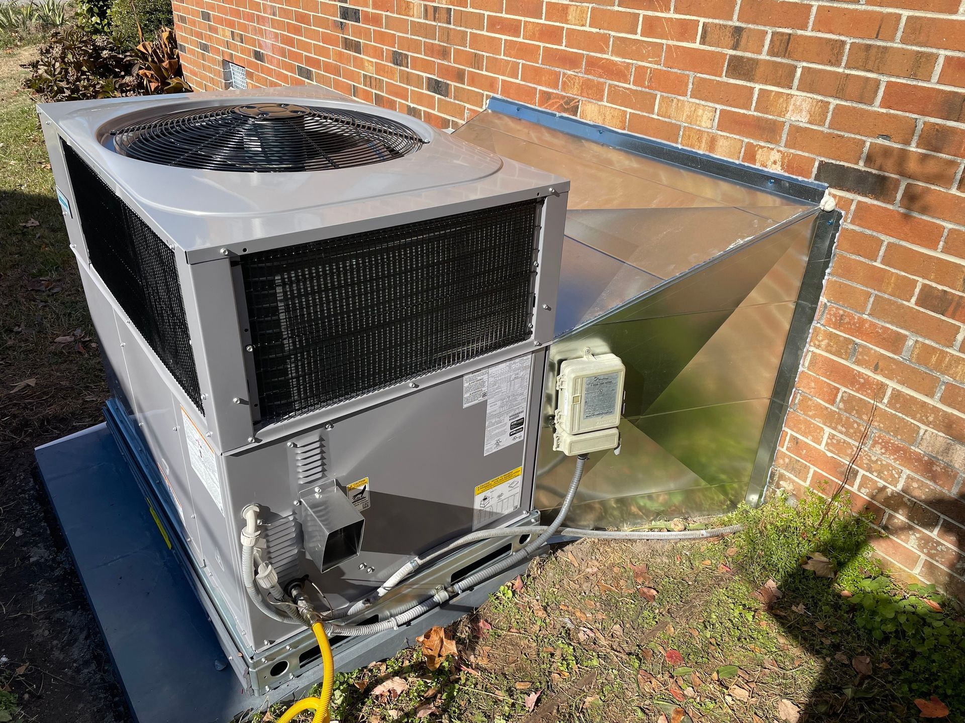 A large air conditioner is sitting outside of a brick building.