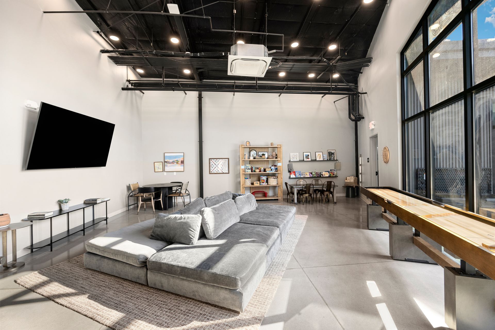 Modern loft-style living room, at Sun Creek Point RV Resort, with gray sectional sofa, wall TV, and large windows with city light views.