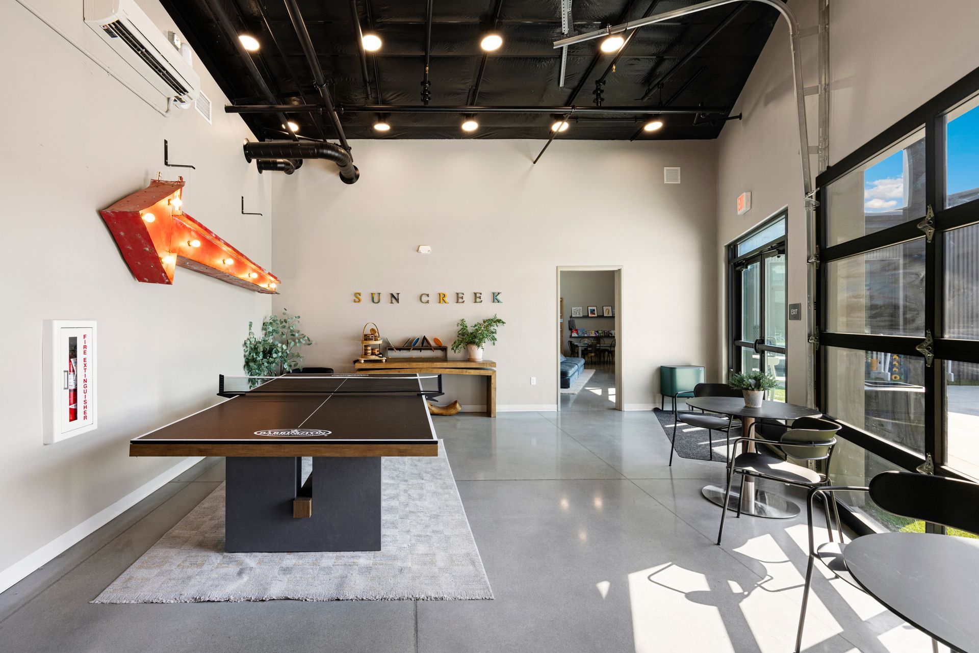 Bright modern game room at Sun Creek Point RV Resort with pool tables, chairs, large windows, and exposed ceiling lights.