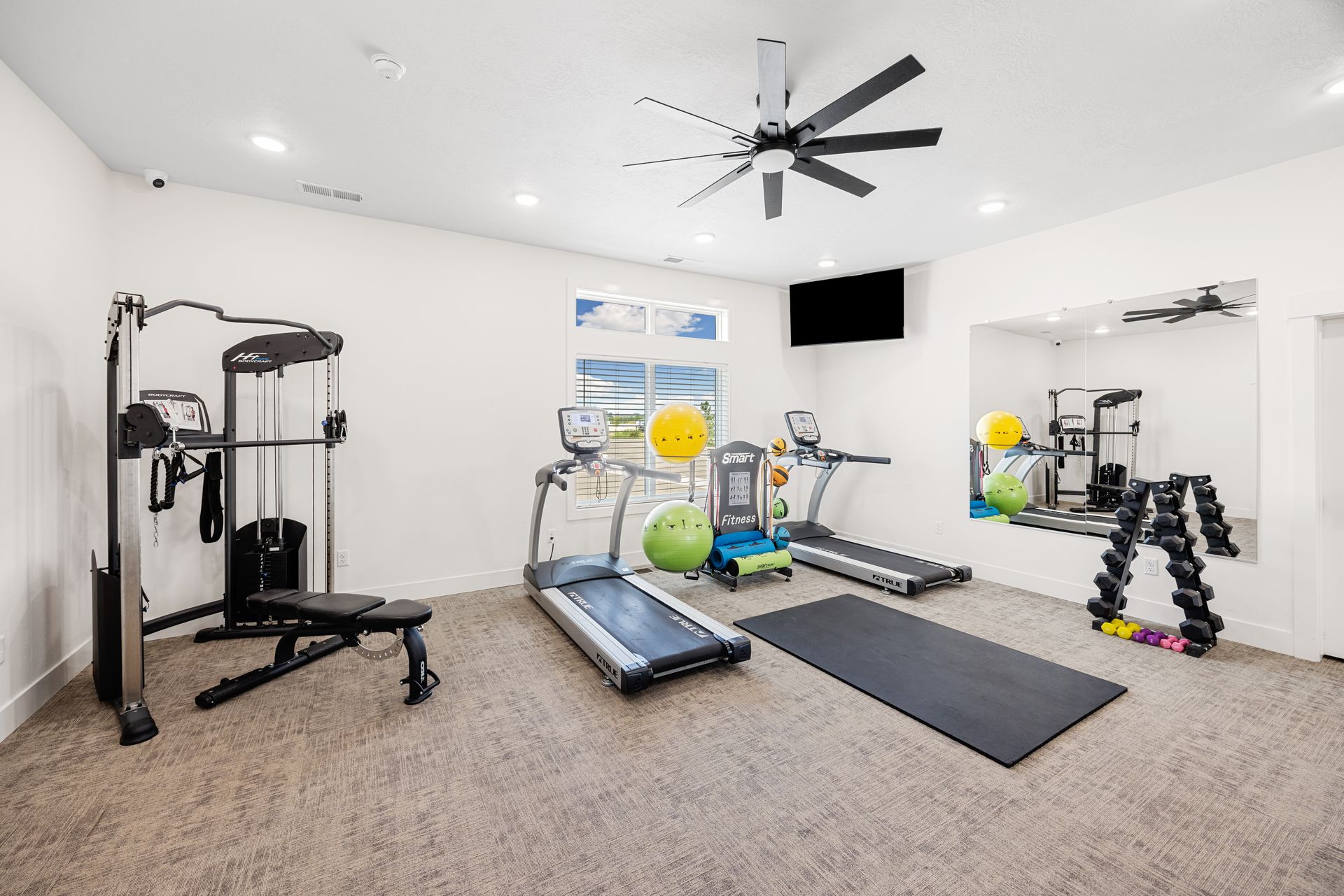 The gym at Idahome RV Resort with treadmill, weight machine, bench, dumbbells, and large wall mirror.