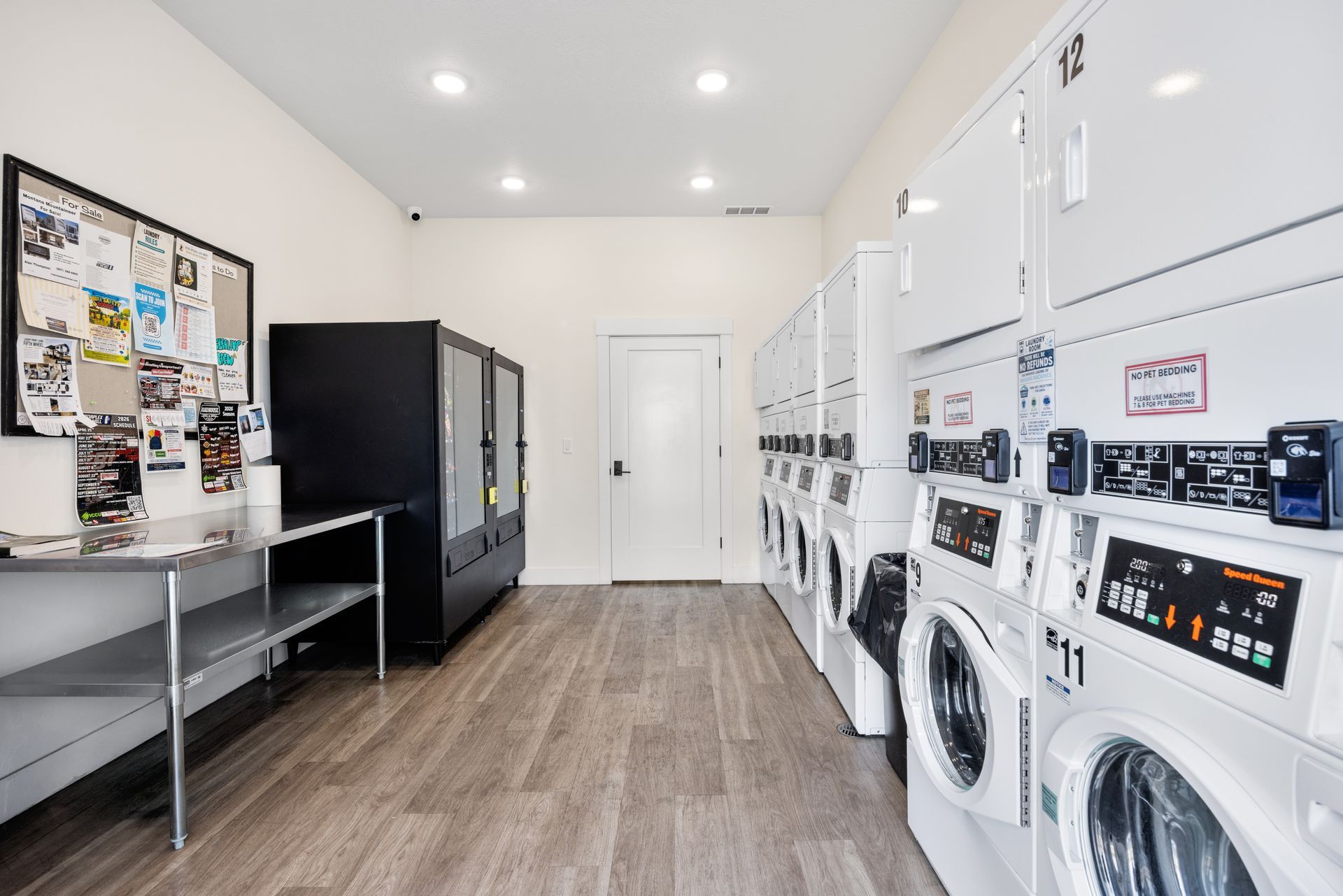 Bright laundry room with rows of white washers, vending machines, and wood floors at the Idahome RV Resort.