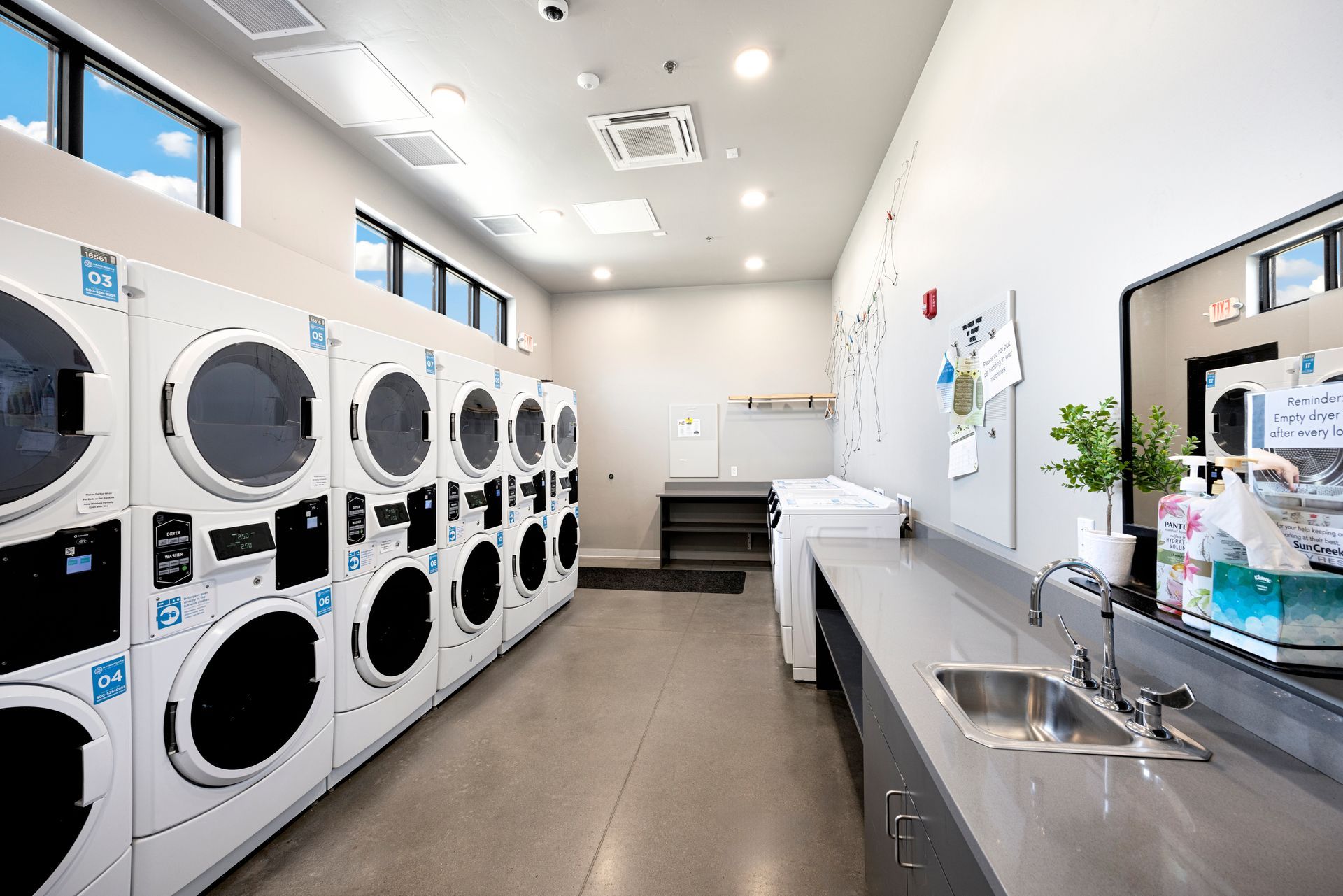 Modern laundromat, at Sun Creek Point RV Park, with rows of white dryers and washers, a folding counter, sink, and bright overhead lights.