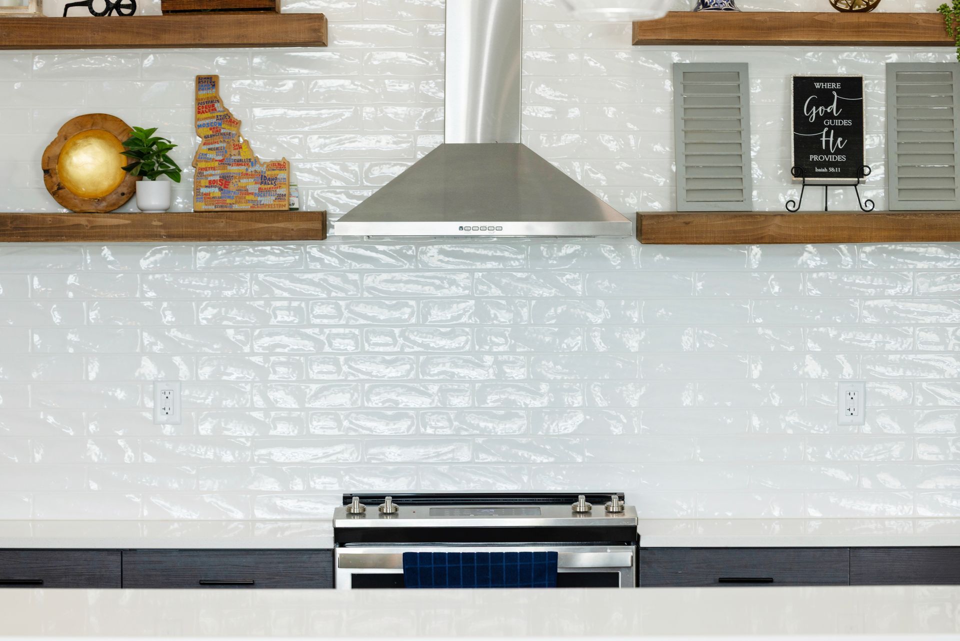 Modern kitchen with white brick backsplash, open shelves, and a stainless steel range hood over a stove at Idahome RV Resort.