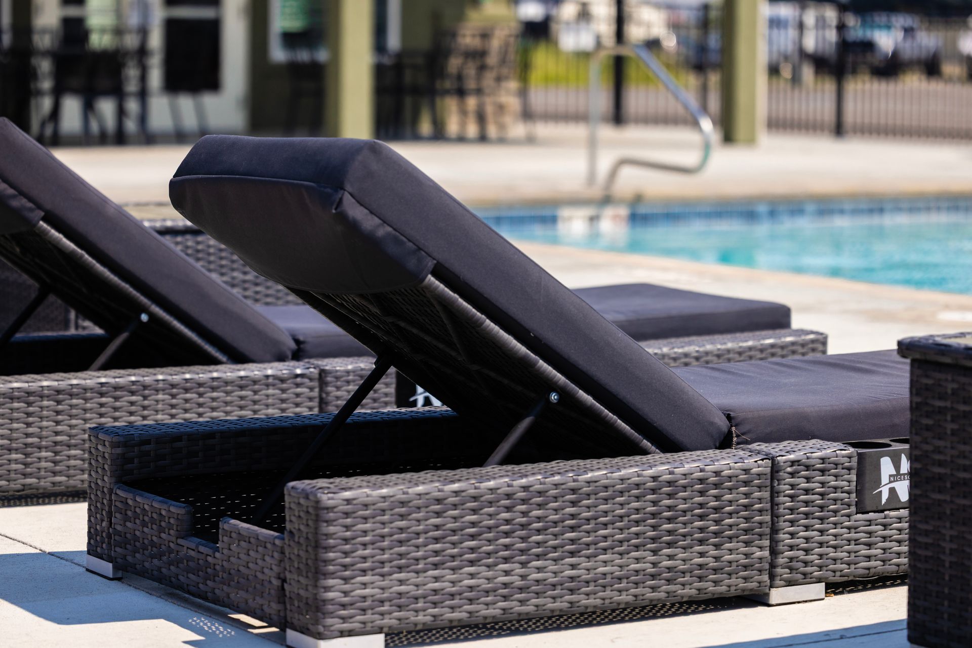 Poolside wicker lounge chair with raised black cushion beside the outdoor swimming pool at Idahome RV Resort.