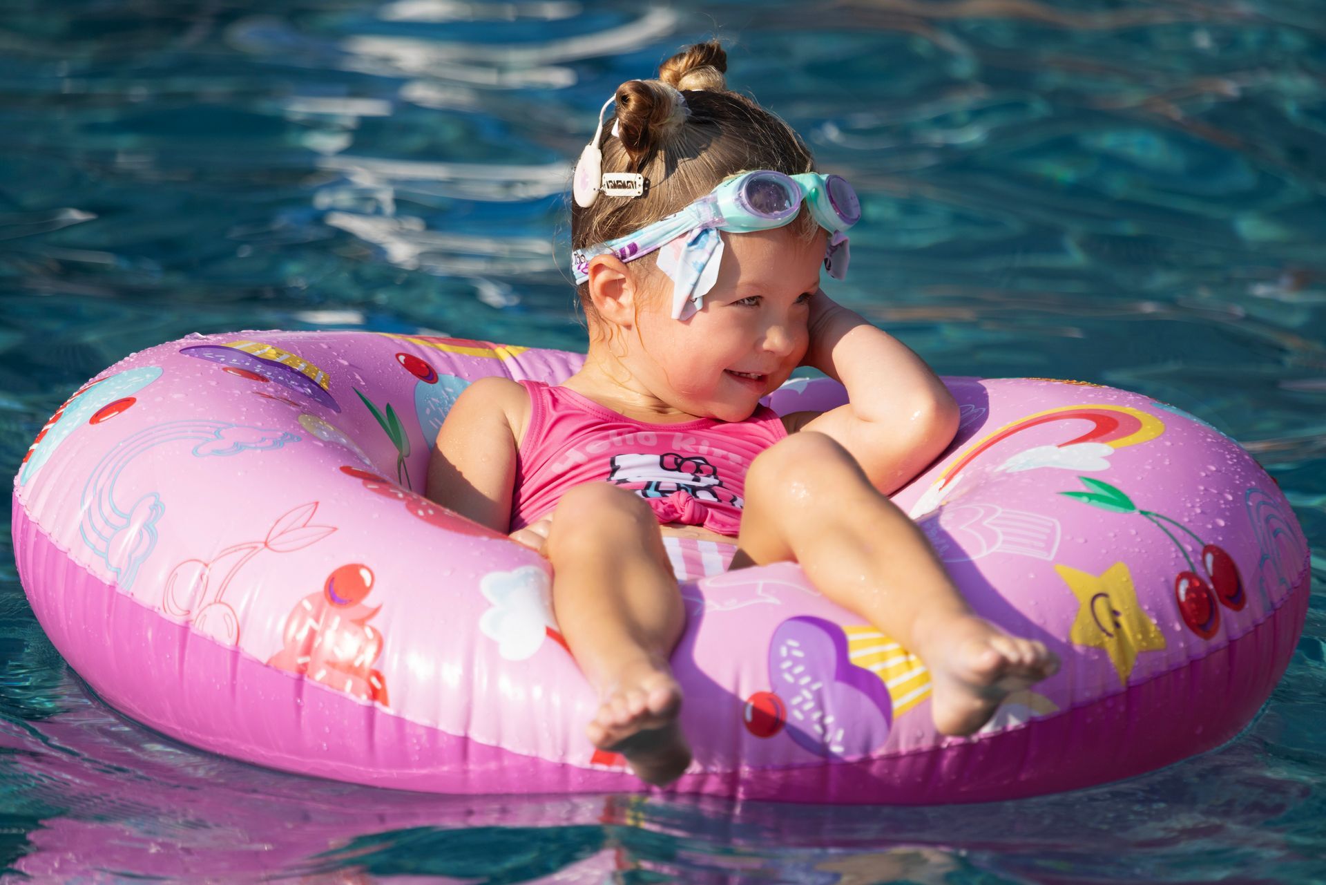 Child floating in a pink donut raft in a swimming pool, wearing goggles and a pink swimsuit at the Sun Creek Point RV Park outdoor pool.