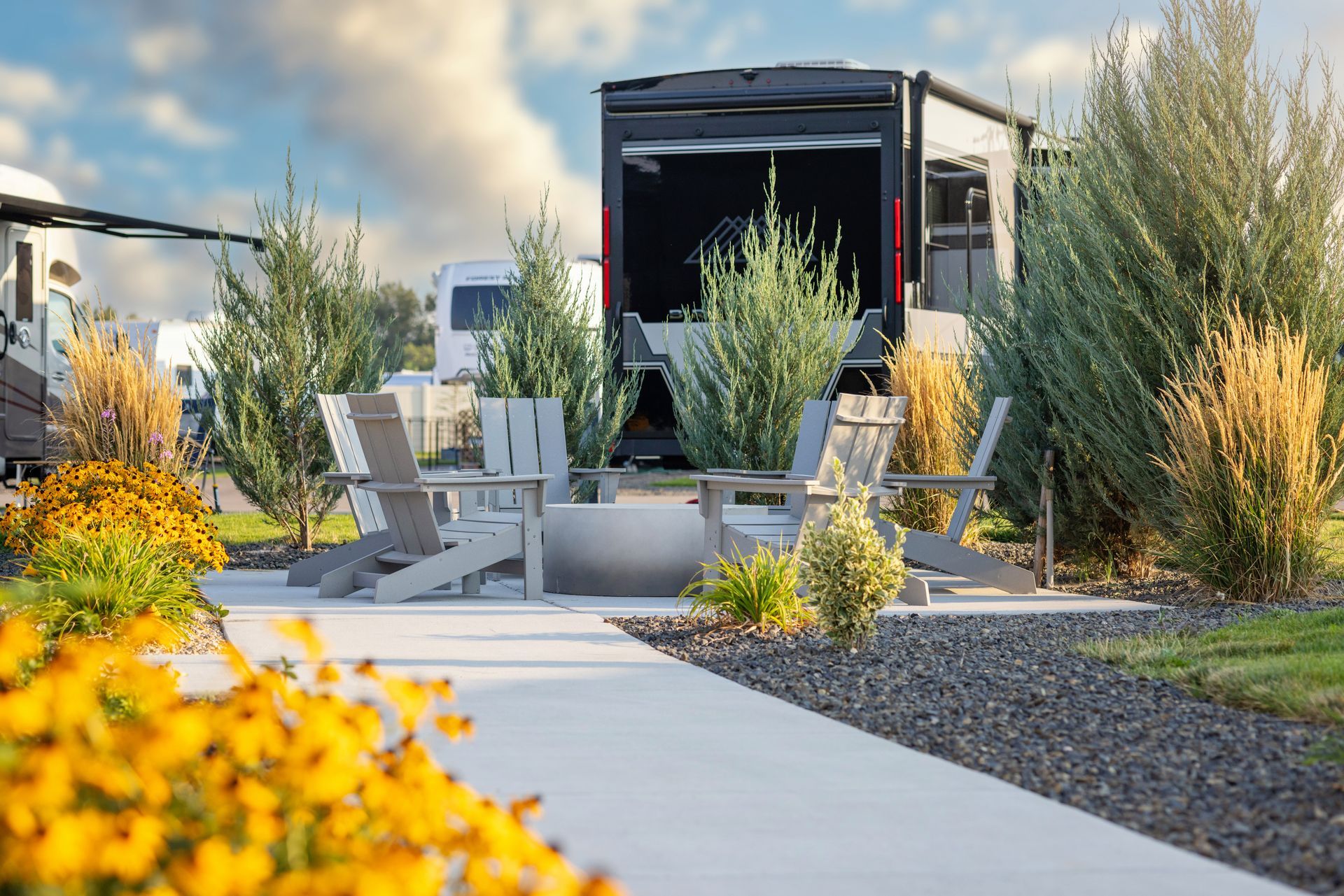 Modern patio with lounge chairs, at Sun Creek Point RV Resort, with potted plants, and a black pergola on a sunny day.