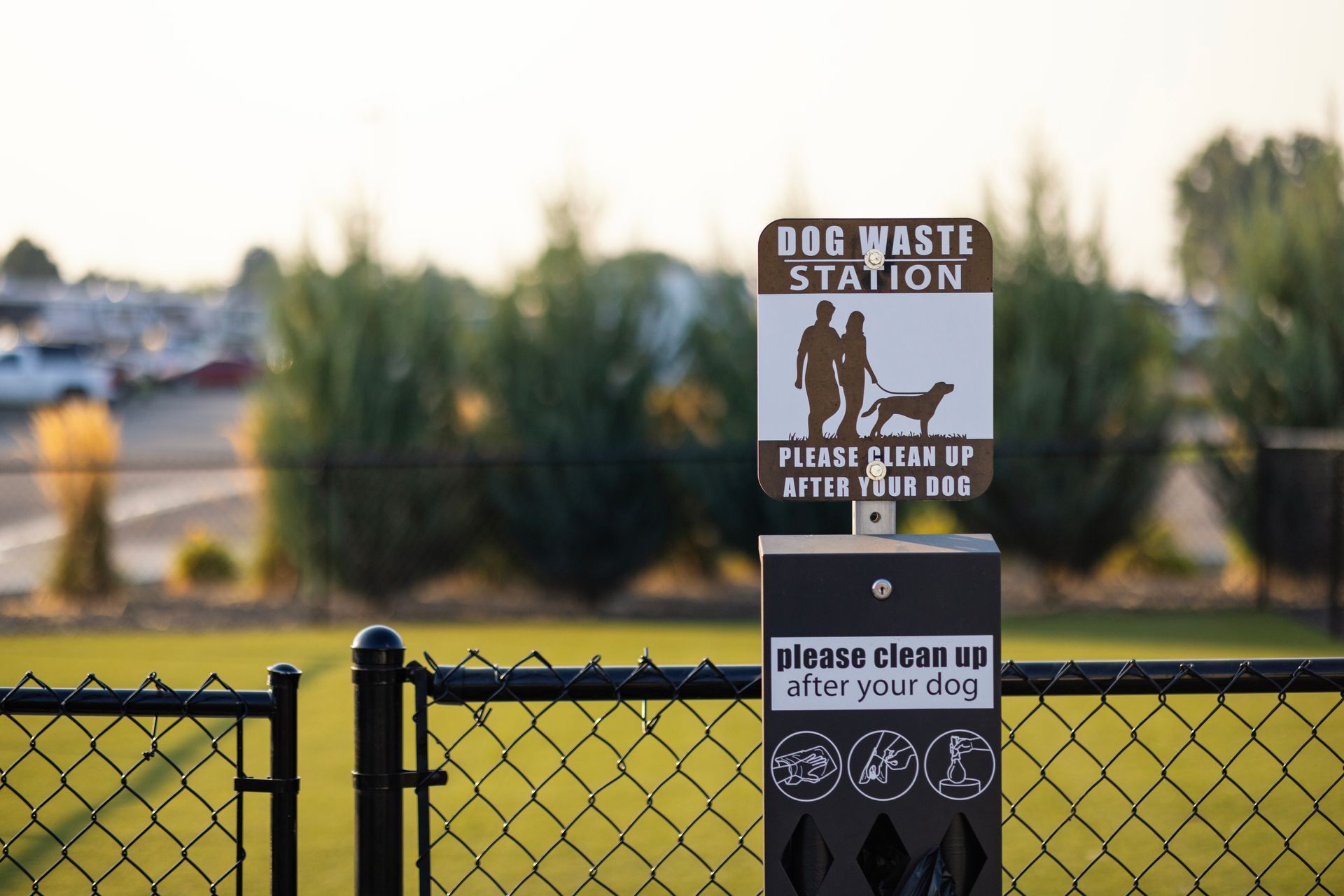 A fenced dog run at the Sun Creek Point RV Park featuring a grassy park, with trees and RVs in the background.