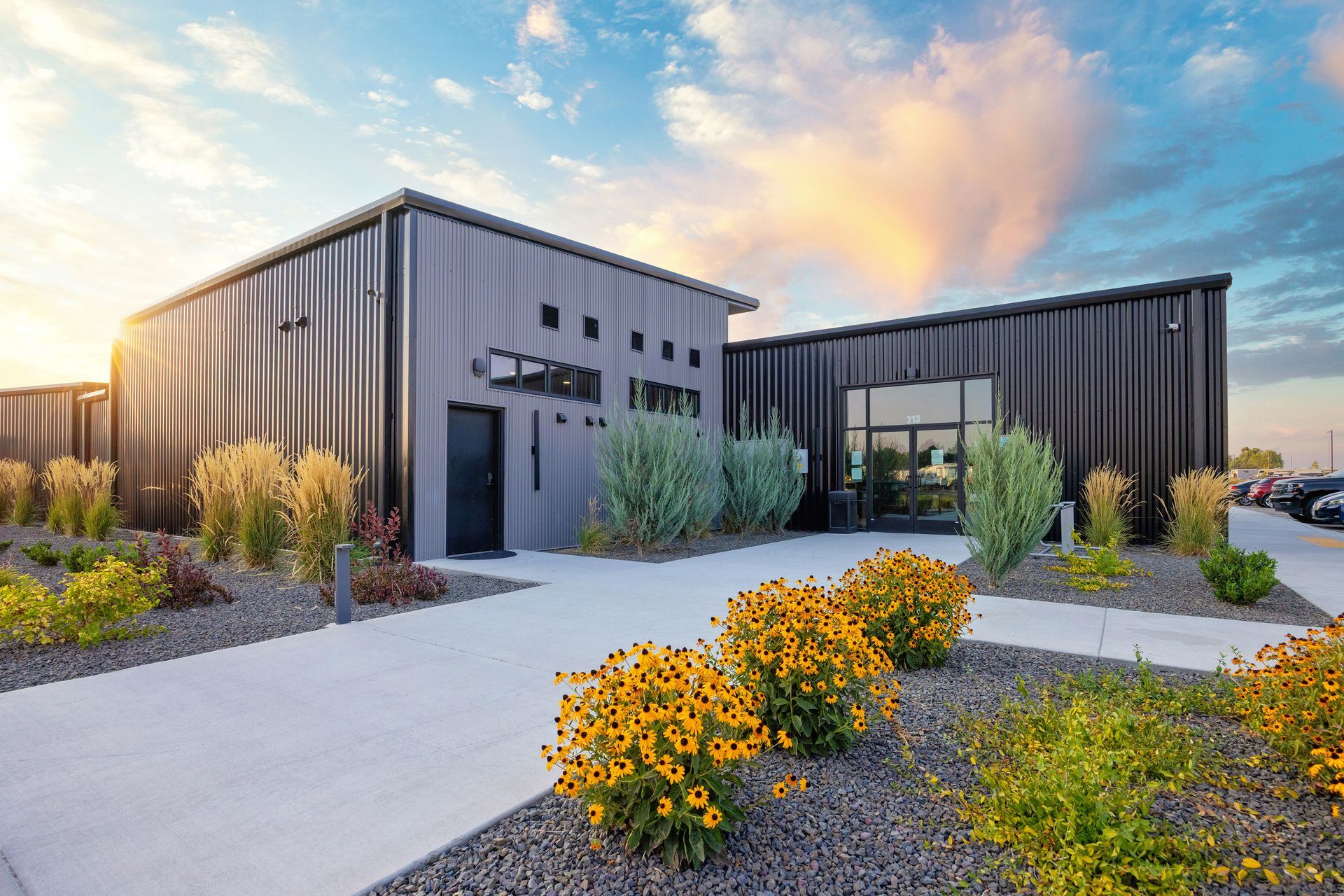 Modern clubhouse at Sun Creek Point RV Resort with landscaped gravel paths and yellow flowers at sunset.