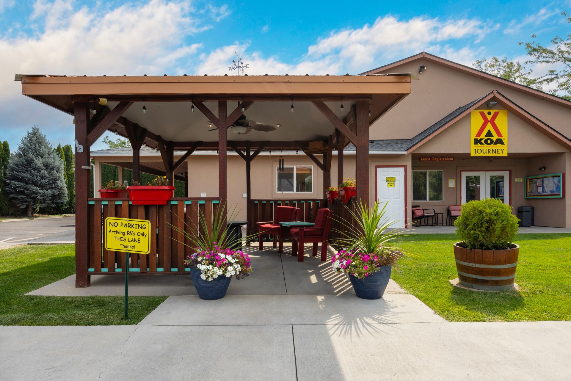 Outdoor patio with wooden pergola, red chairs, flowers, at the Boise Meridian KOA.