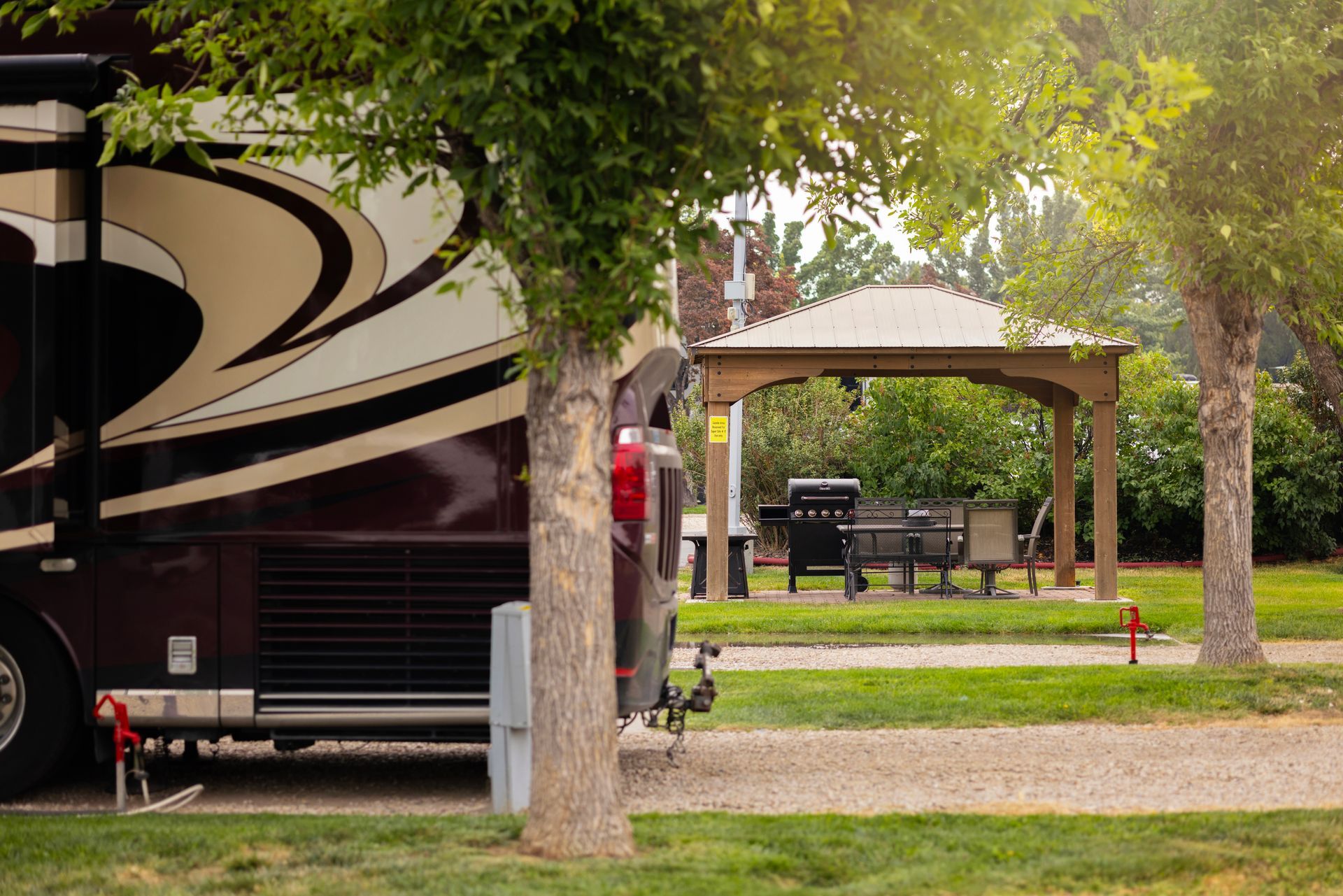 Large RV parked at the Boise Meridian KOA in a grassy campground with trees and a gazebo in the background
