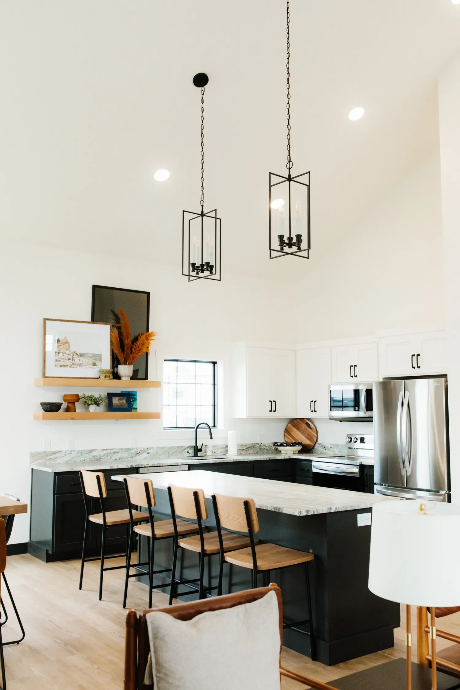 A modern kitchen, at Center Point RV Resort, with a black island, white cabinets, bar stools, and hanging pendant lights.