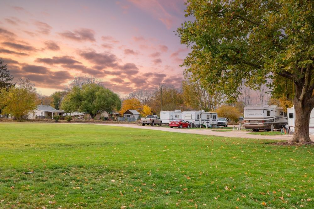 Mason Creek RV Park with green grass, RVs, and autumn trees under a pink sunset sky.