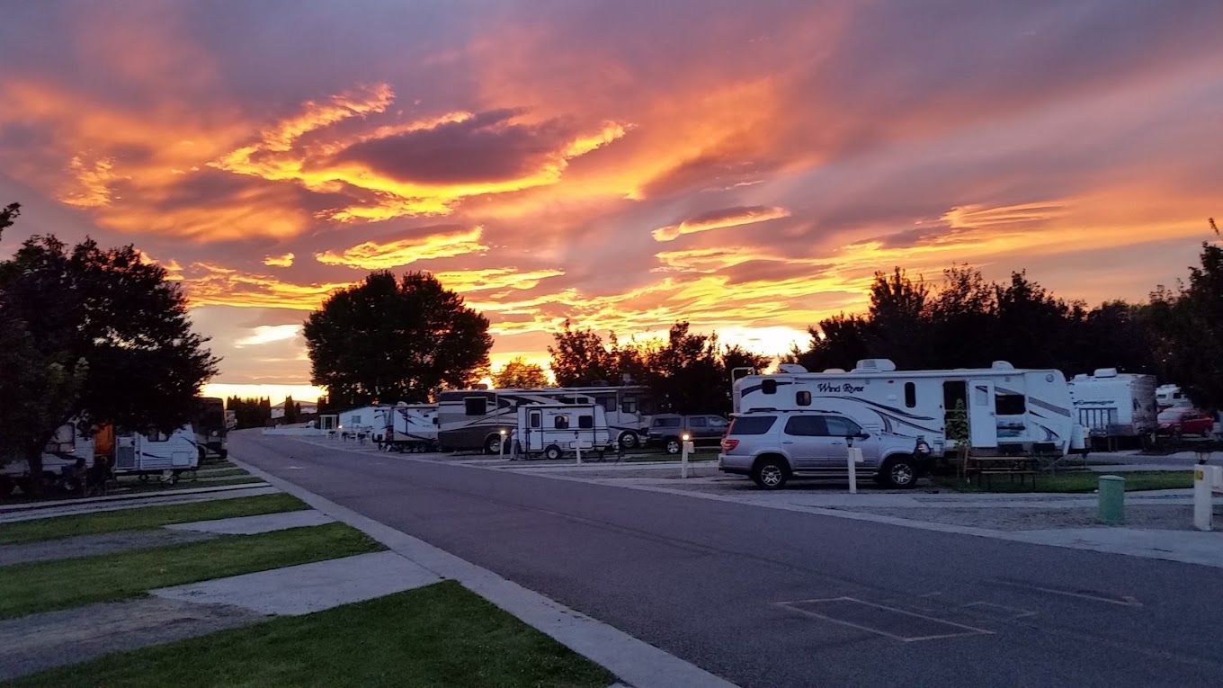 Sunset over the Pasco Tri-Cities KOA with RVs, trees, and dramatic orange-purple clouds.