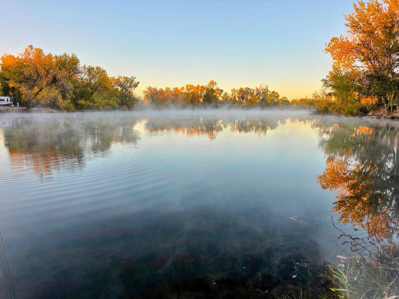 Calm misty lake at sunrise, with autumn trees reflected in the still water at Lake Point Campground.