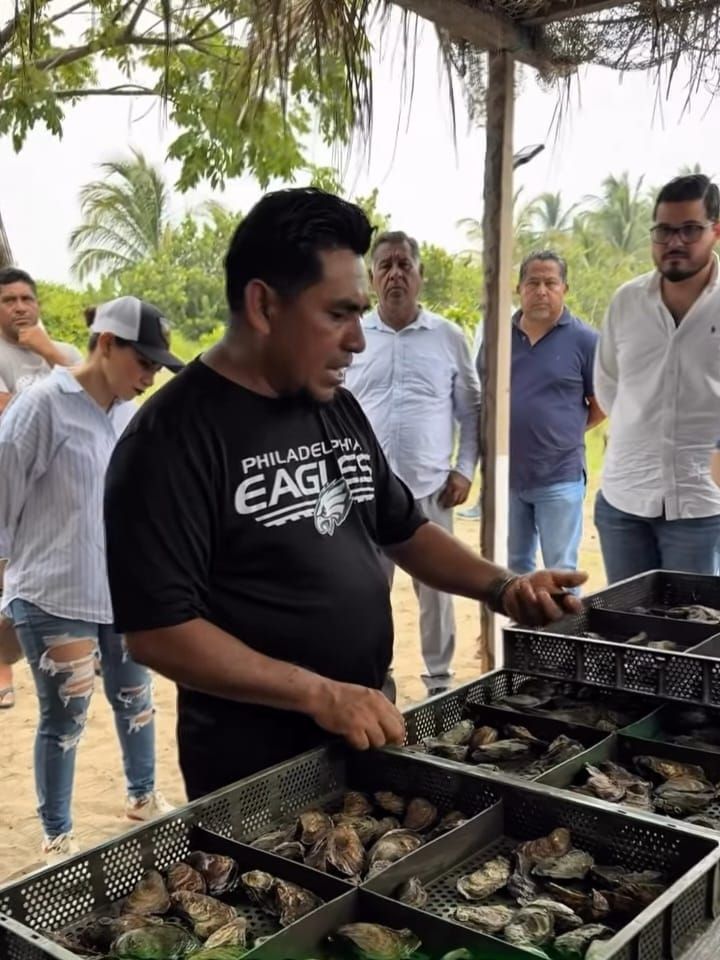 Man grilling shellfish outdoors at a beachside barbecue under a thatched roof