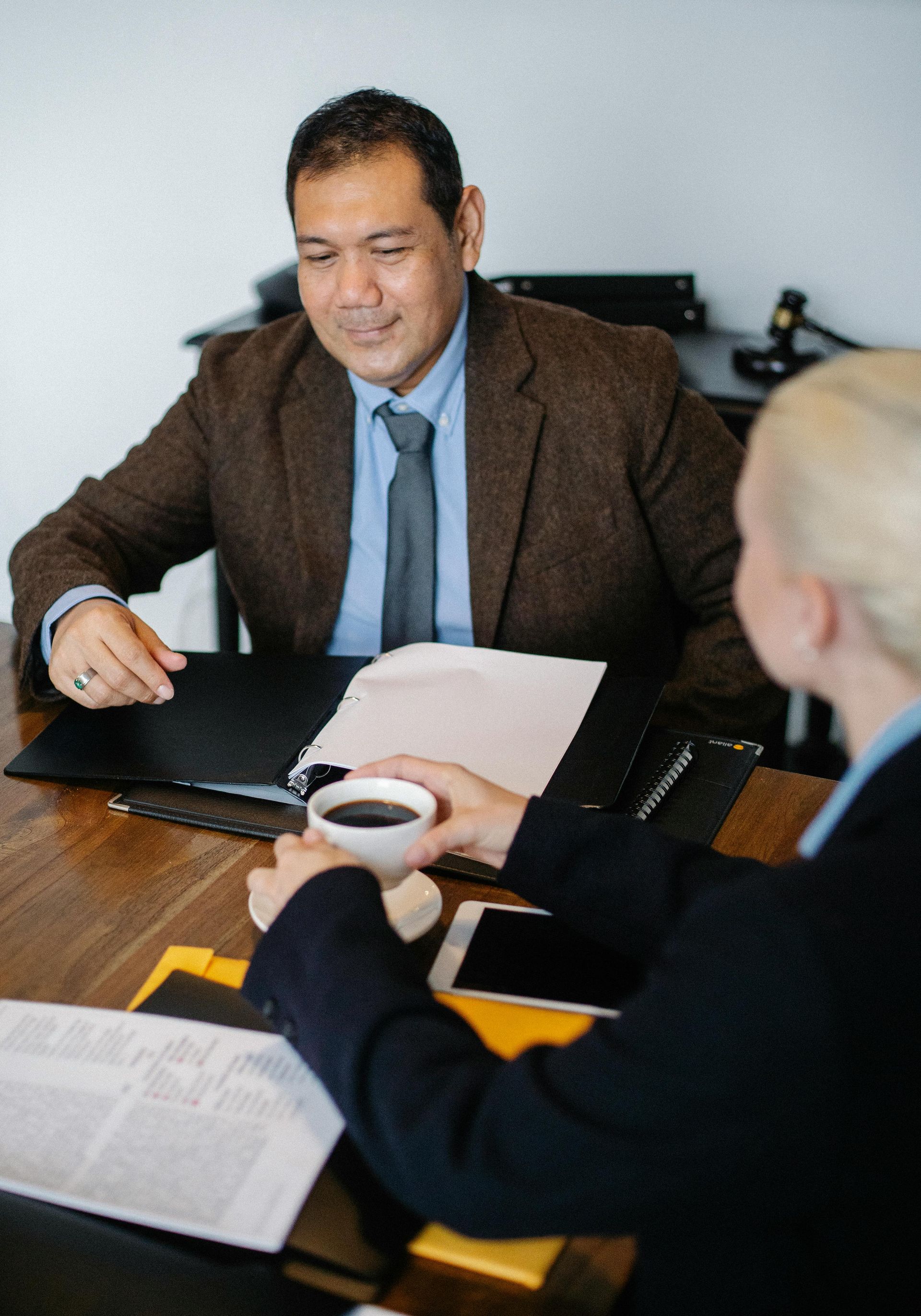 Three people in a meeting, with documents and a coffee cup on a conference table.