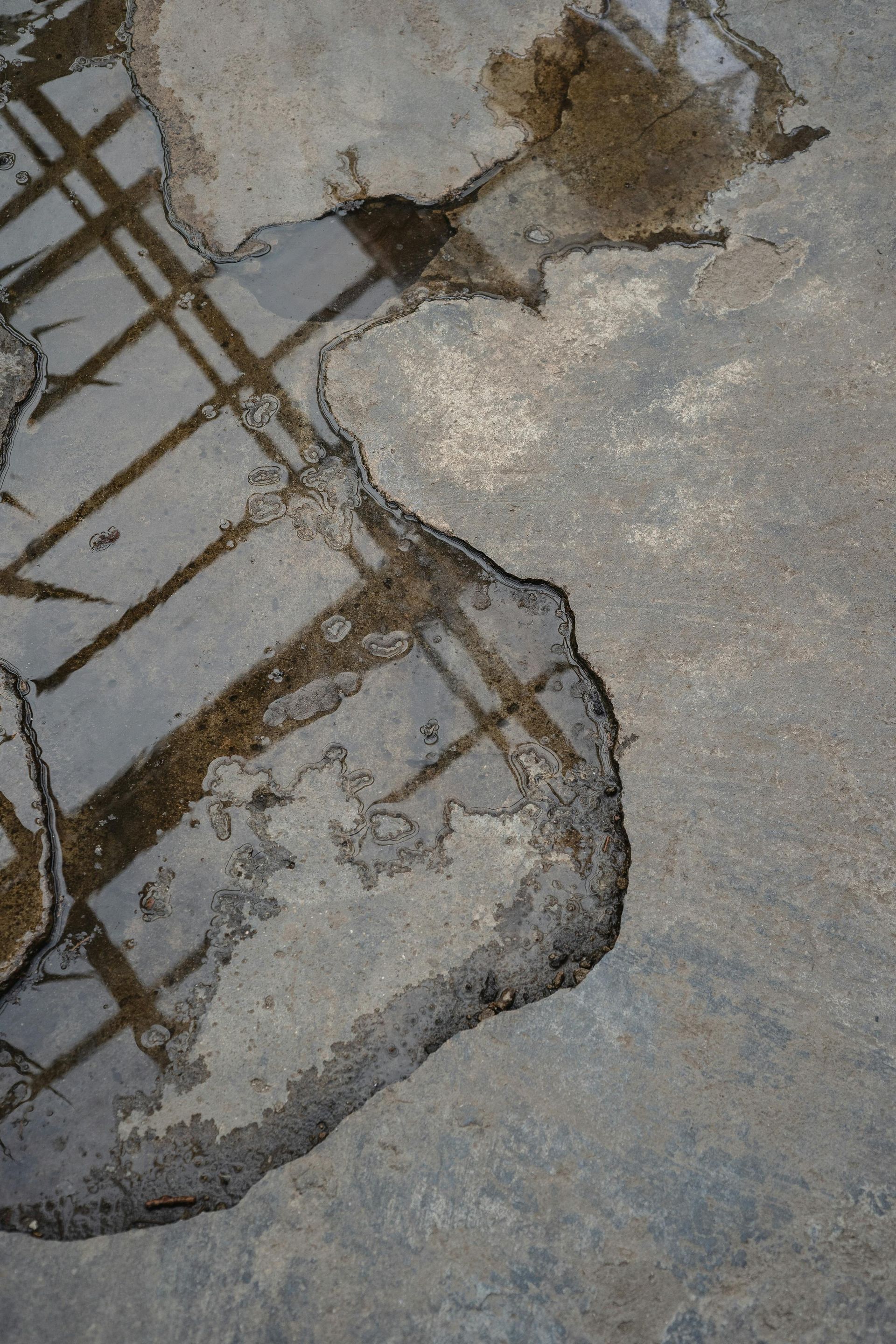 Cracked concrete pavement with exposed rebar and a broken patch on a gray surface