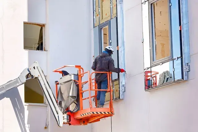A man is standing on a lift working on a window's building.