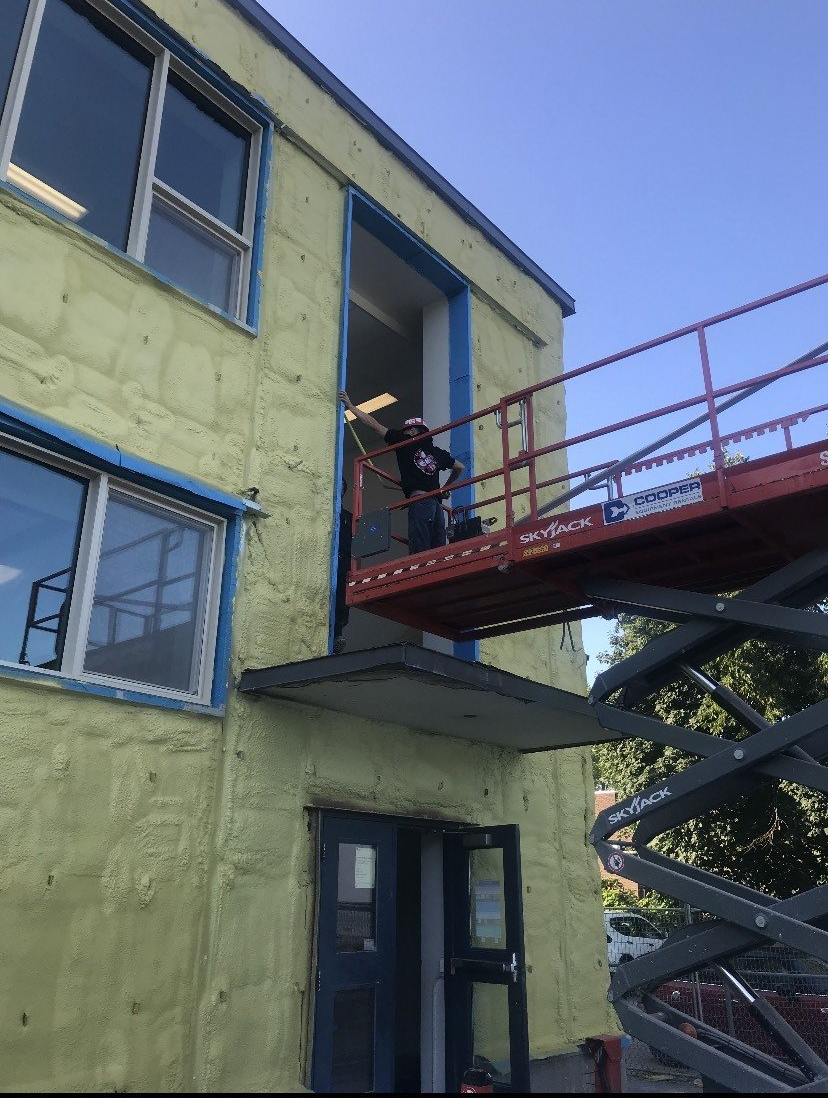 A man is standing on a scissor lift on the side of a building