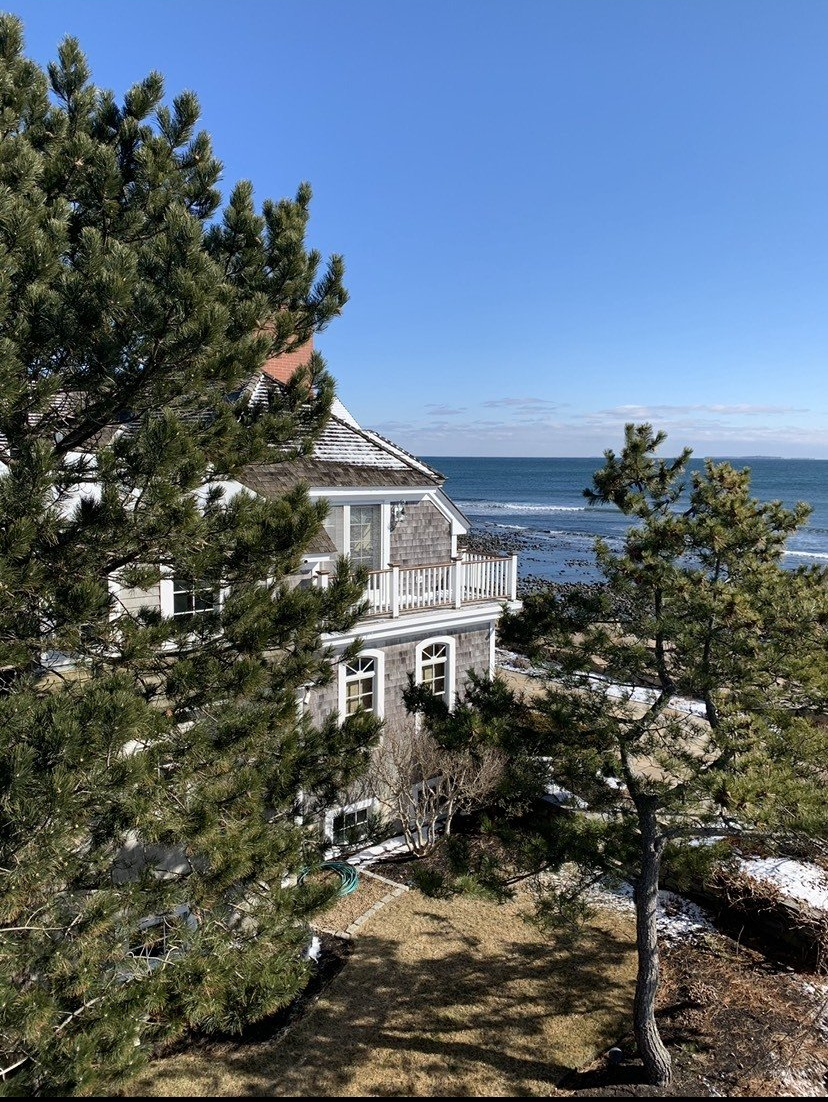 A house on a hill overlooking the ocean with trees in front of it.